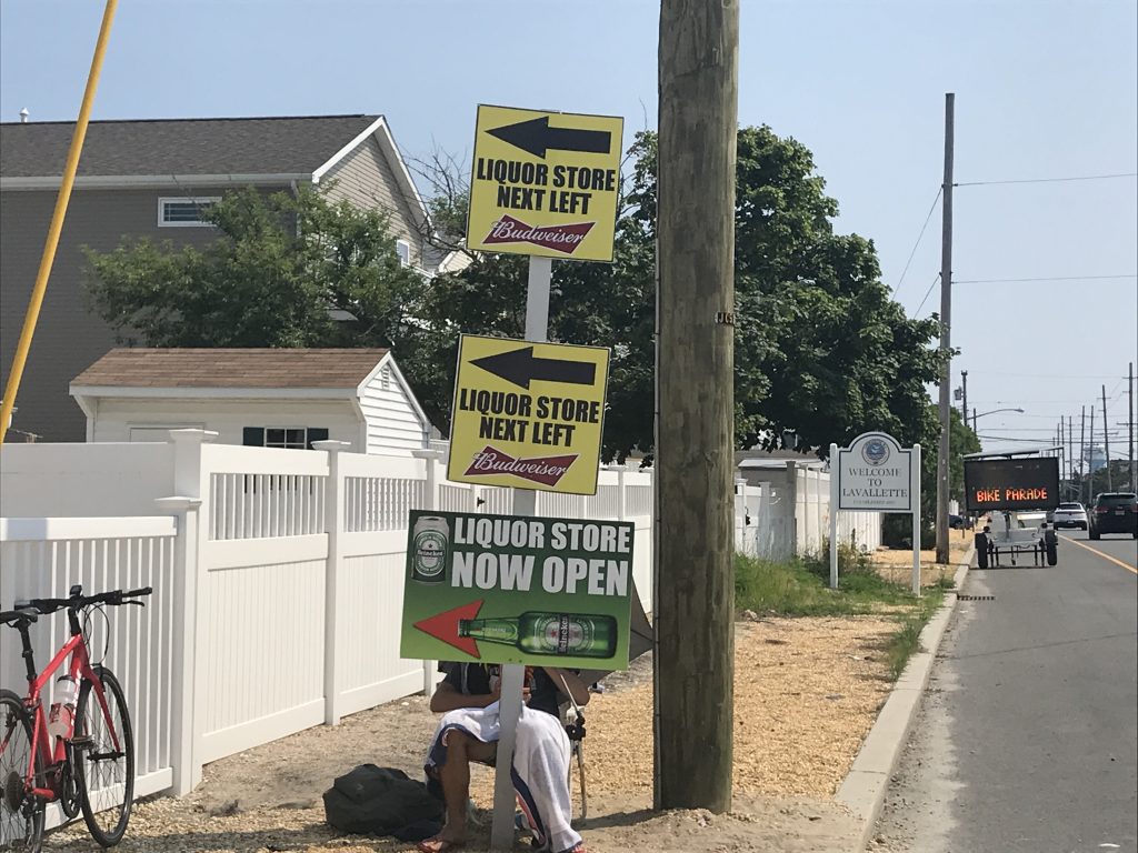 A liquor store employee holds a sign on Route 35 advertising the business. (Photo: Daniel Nee)